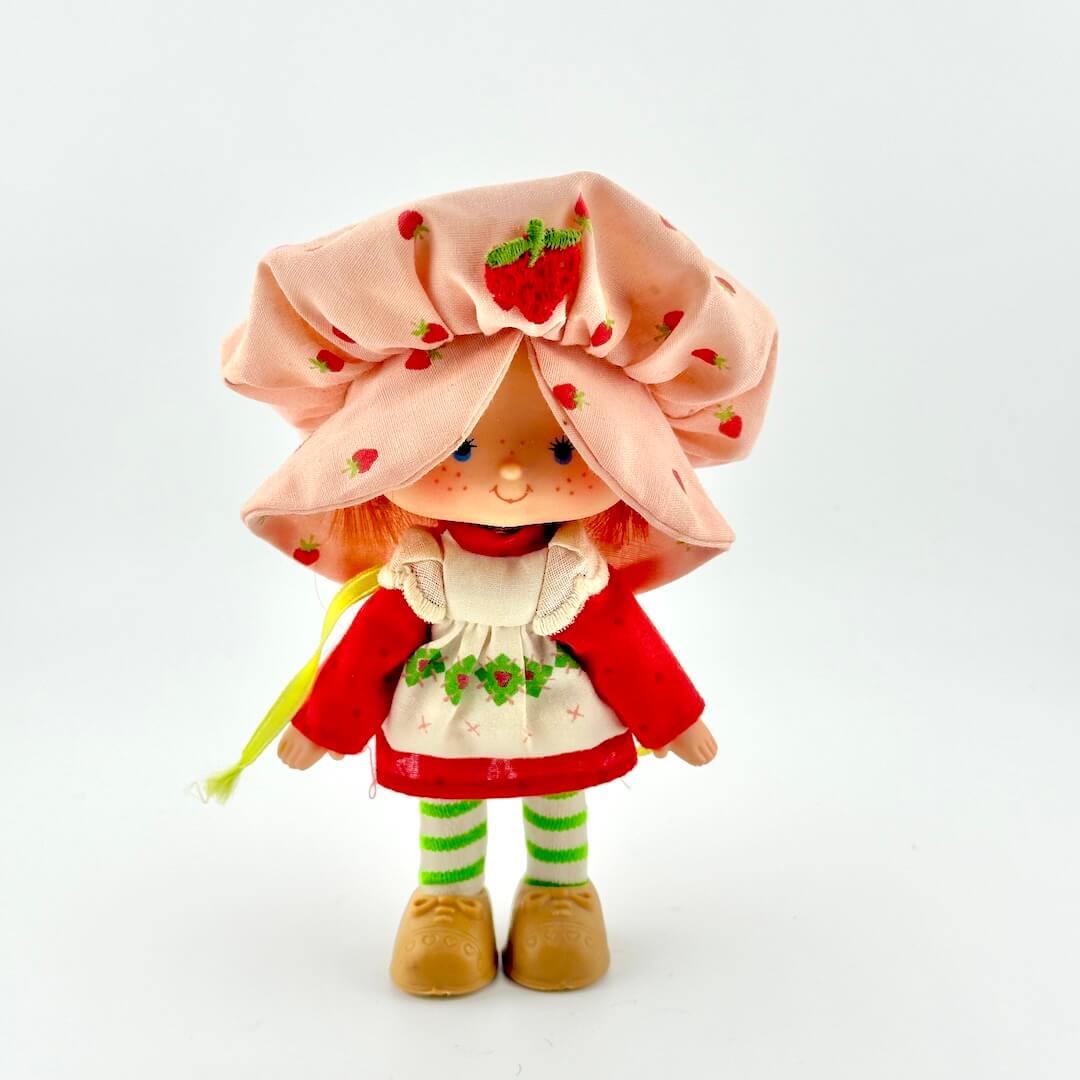 Toy doll with pink hat and red dress against white background.