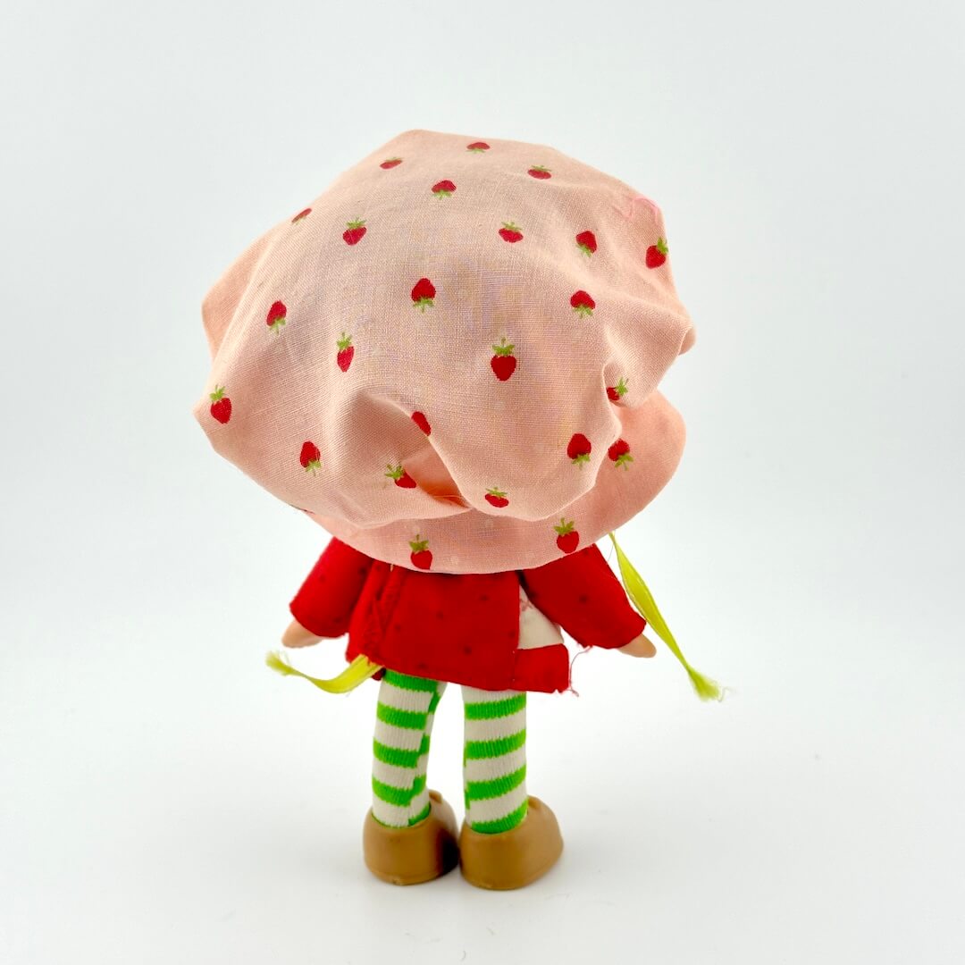 Toy doll with red dress and pink hat against white background.