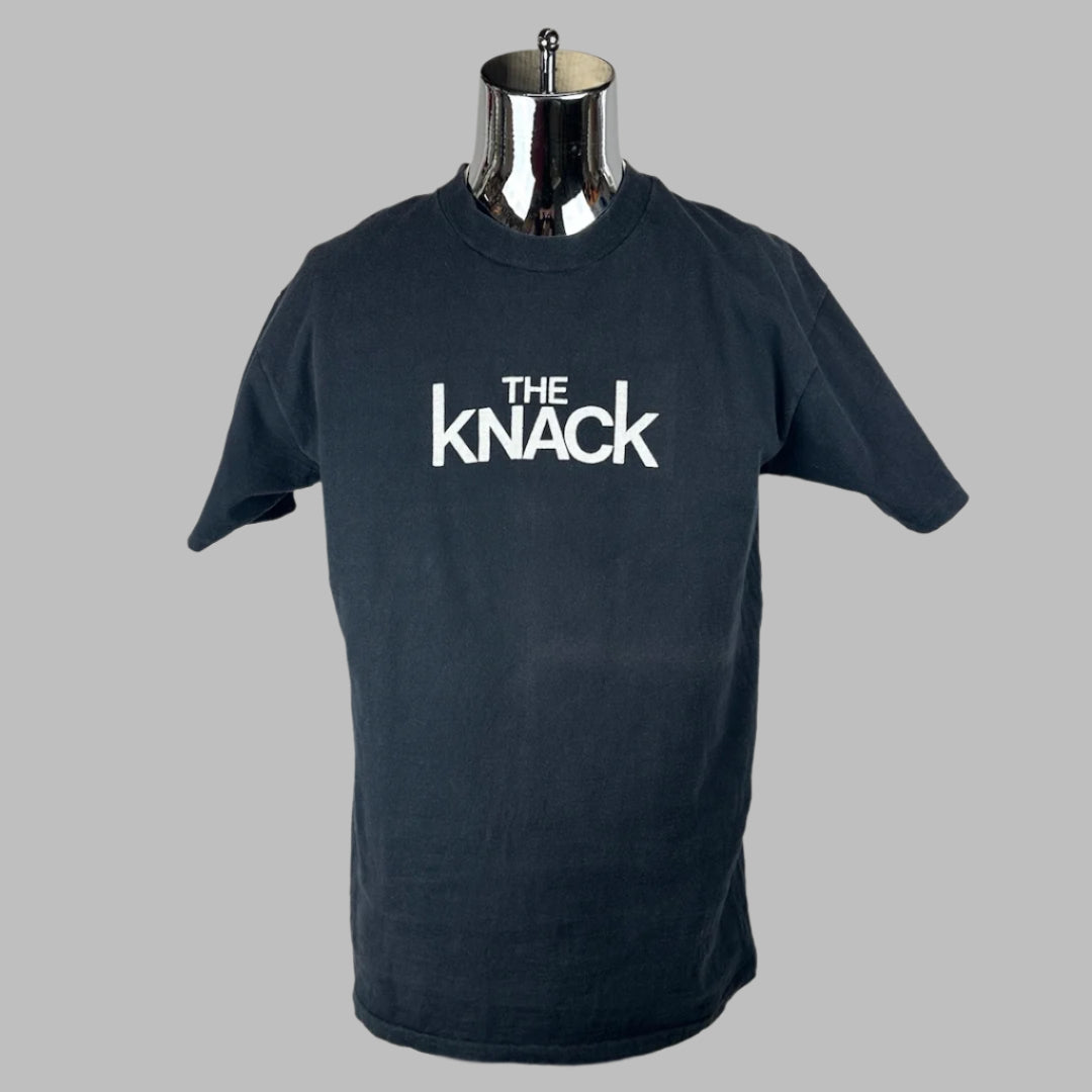 Black crew neck, short sleeved t-shirt with white text in center of chest, "THE KNACK."