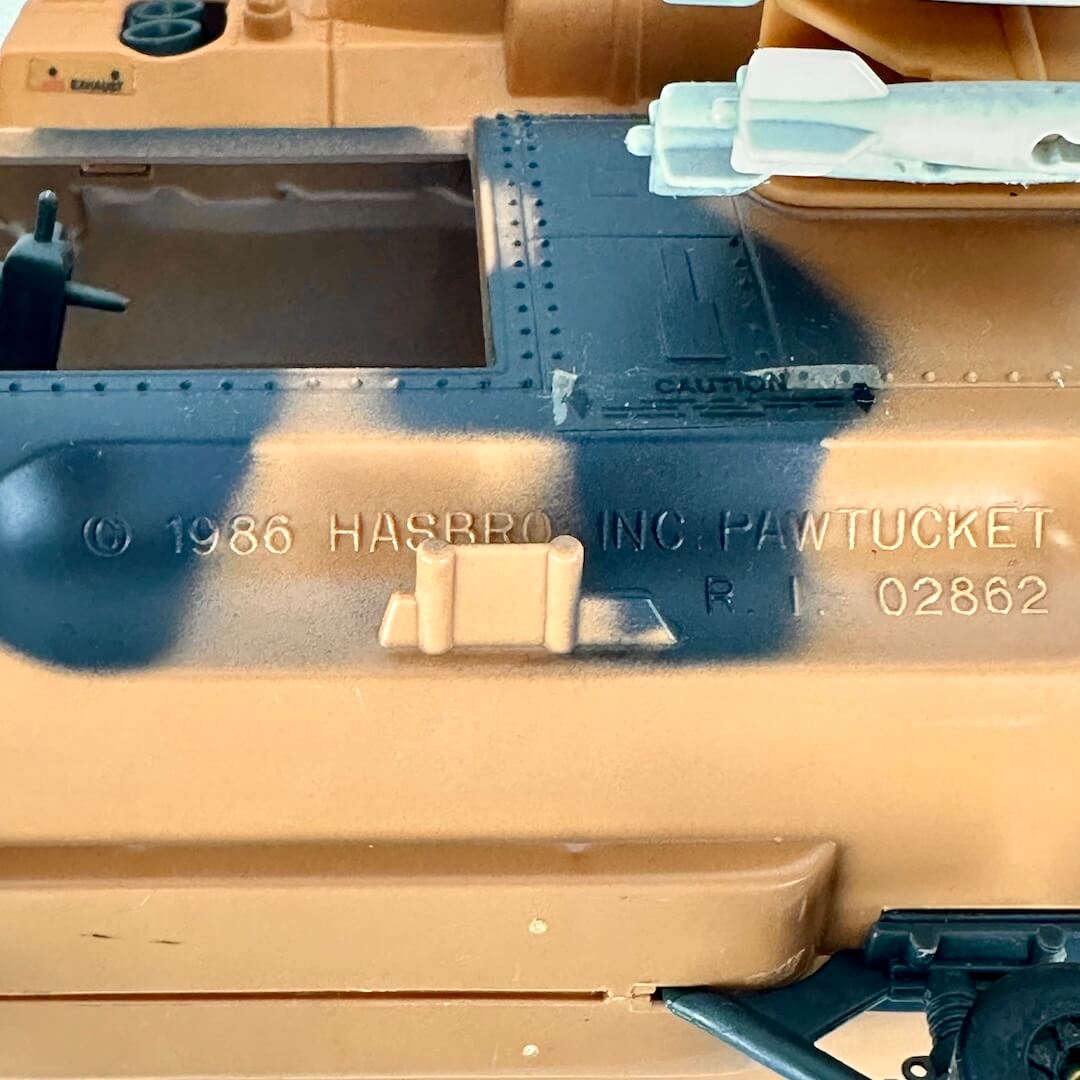 Close-up of a model vehicle body panel in tan plastic with a dark gray spray-painted section, embossed Hasbro copyright text.