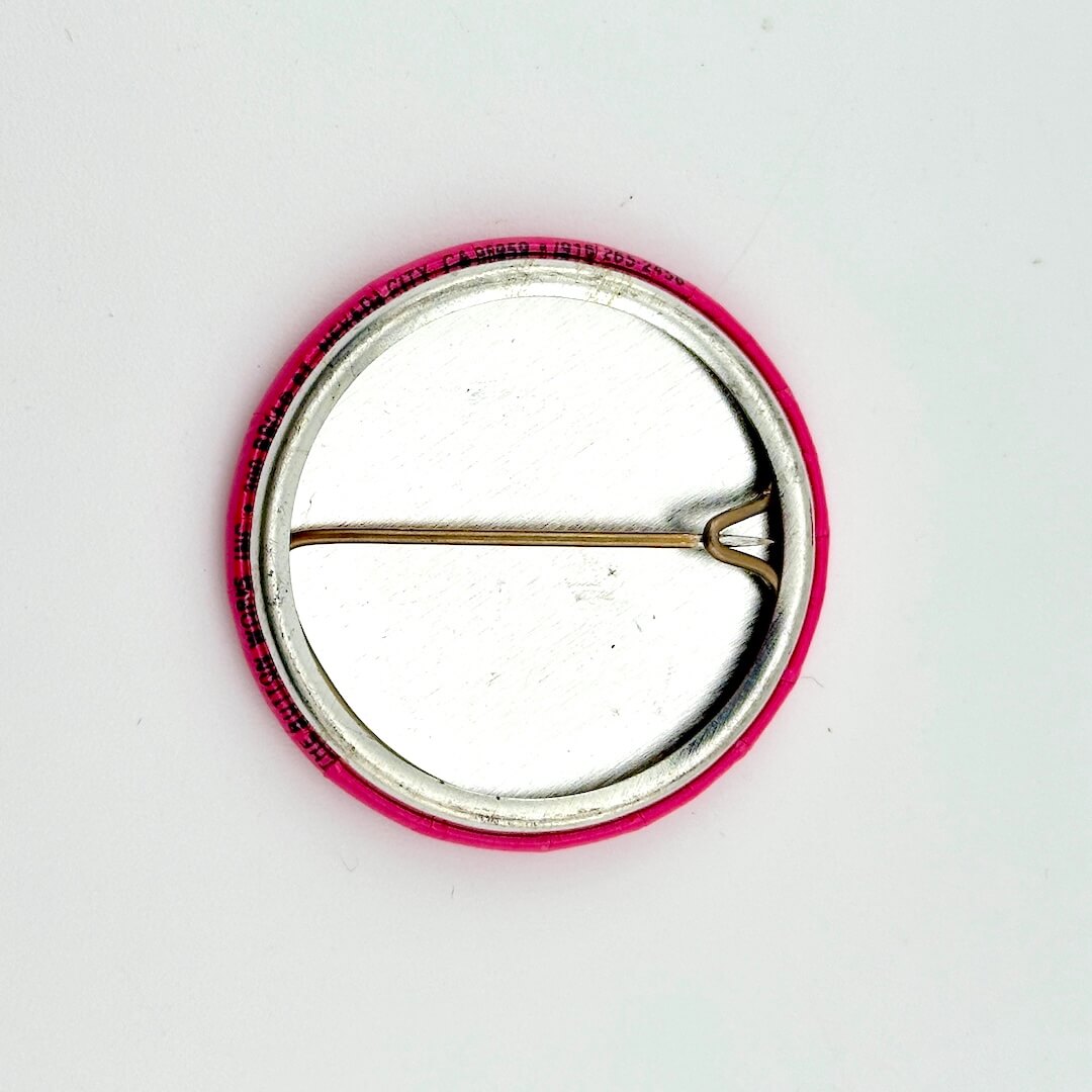 Circular pin with pink border and silver center on a white background