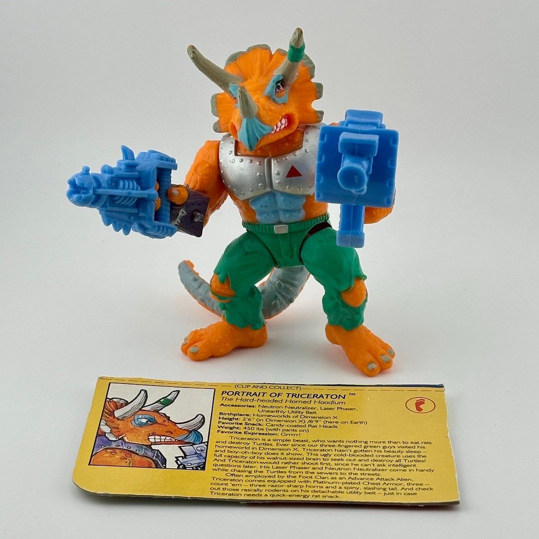 Anthropomorphized triceratops wearing silver armor chest piece, green pants, holding two large, blue guns. Front.