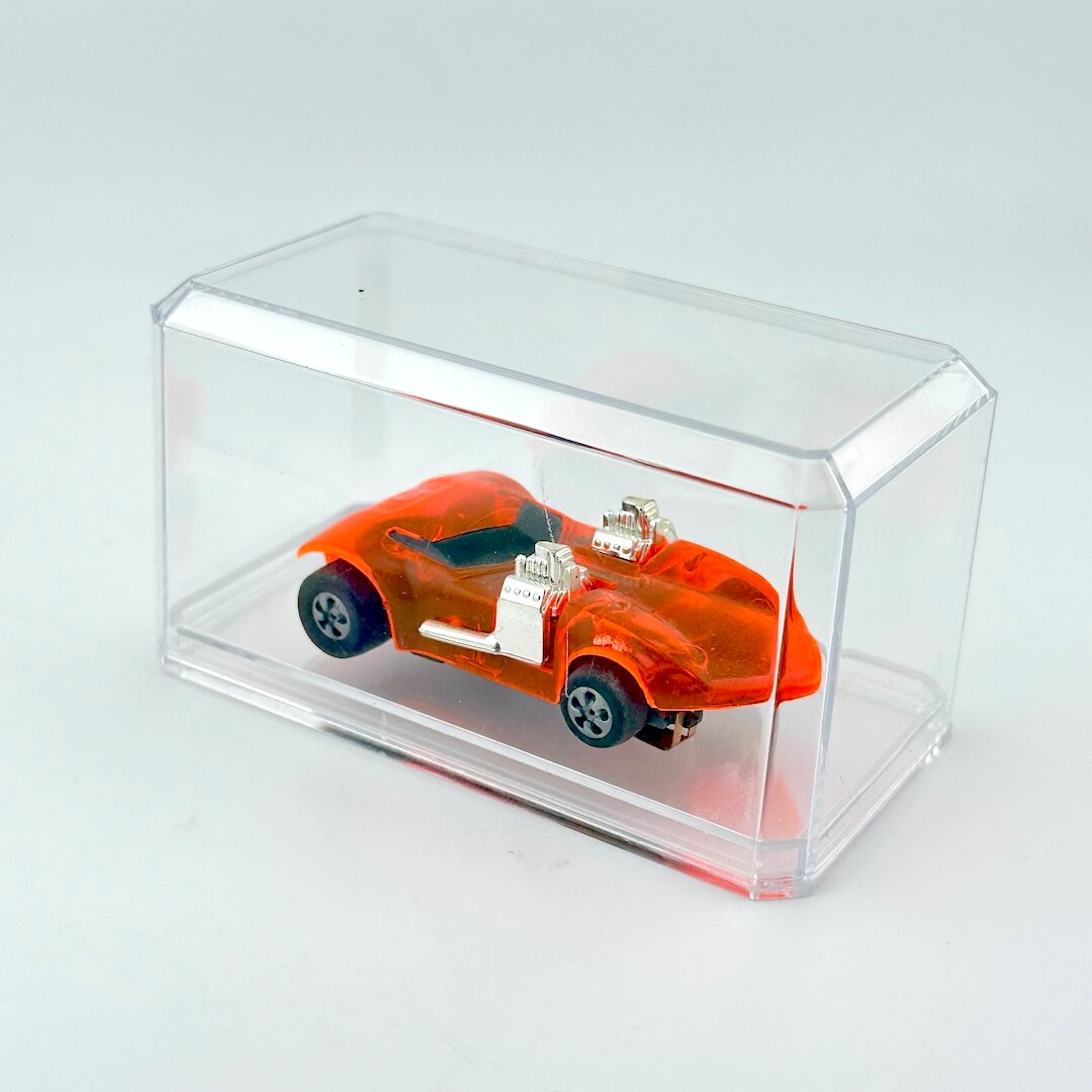Small orange car model inside a clear acrylic box on a light gray background