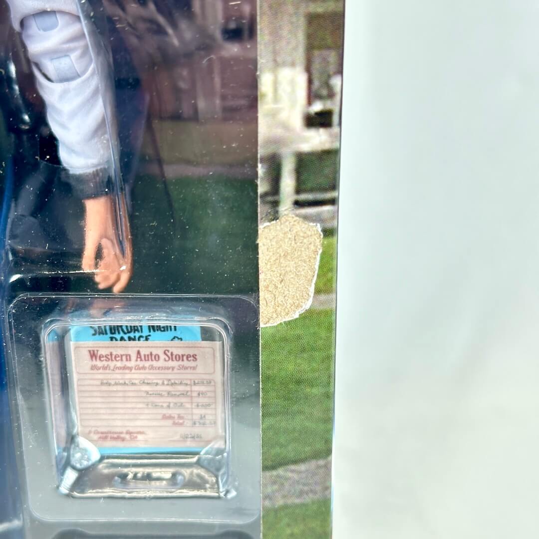 Action figure in a clear packaging with a label on a reflective surface