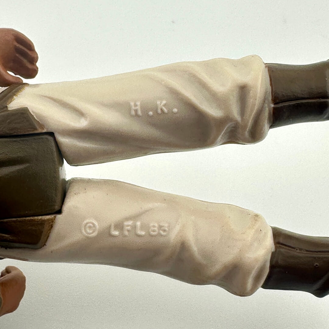 Close-up of a figure's legs with 'H.K.' and 'LFL83' branding on a plain background
