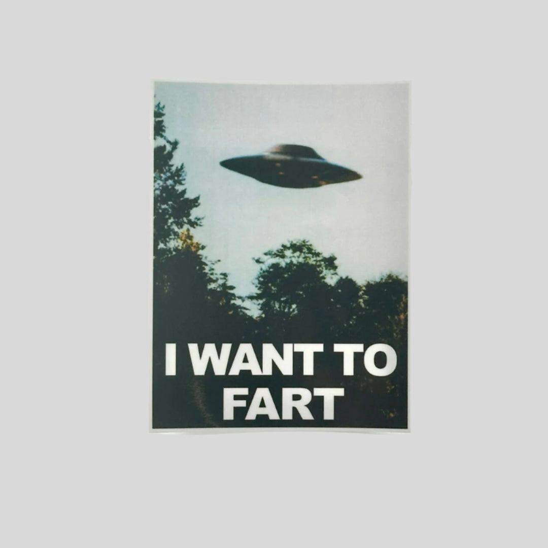 X-Files parody sticker reading "I want to fart" under flying saucer above treeline.