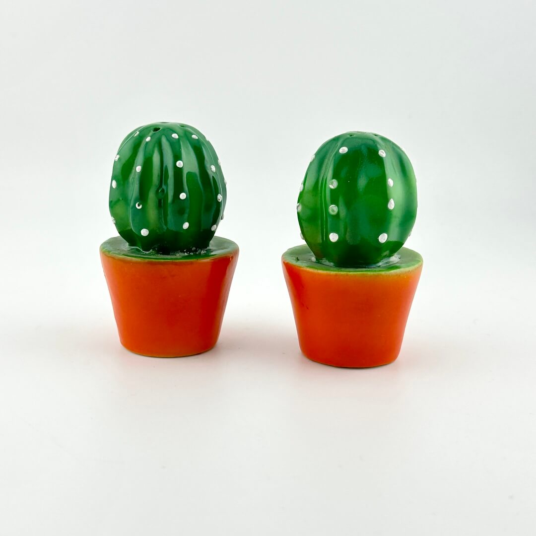 Two green cactus-shaped salt and pepper shakers with orange bases on a white background