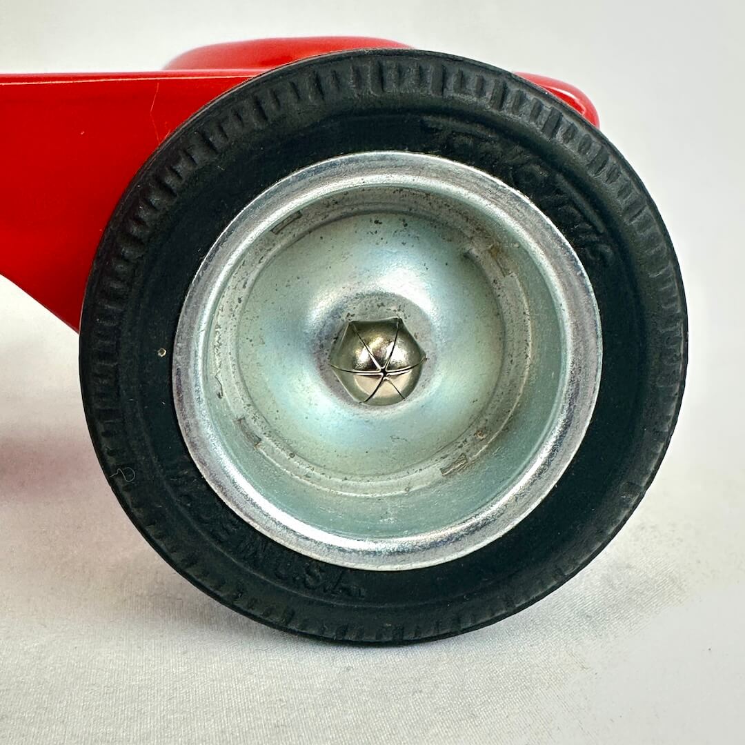 Close-up of a red toy truck wheel with black tire on a white background