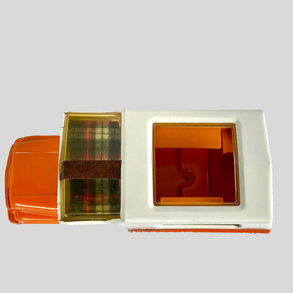 Orange and white toy truck with camper top with a plaid blanket in attic on a white background
