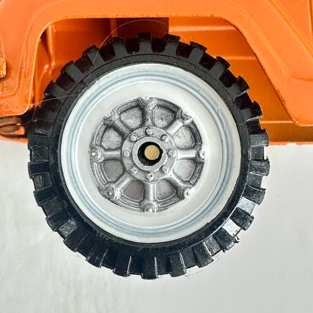 Close-up of a toy truck wheel with black tread and silver hub on an orange vehicle.