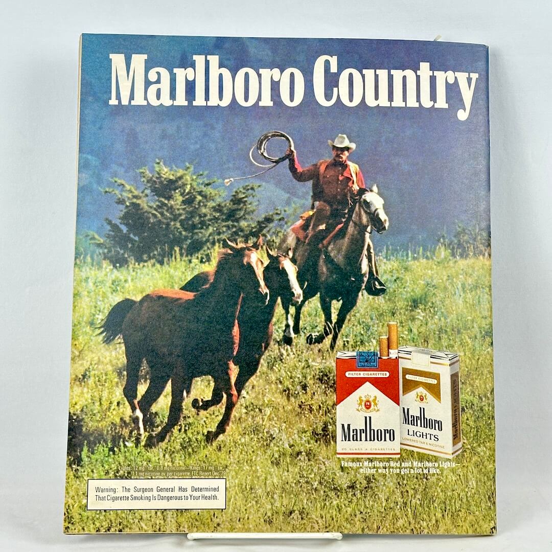 A vintage Marlboro Country cigarette advertisement featuring a cowboy riding a horse chasing other horses. 