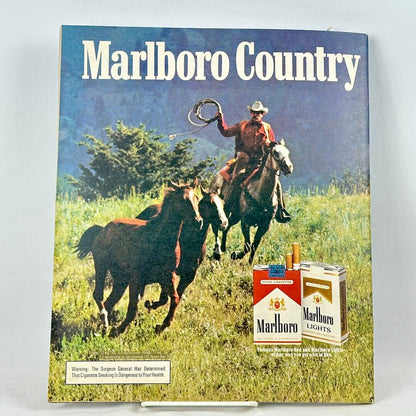A vintage Marlboro Country cigarette advertisement featuring a cowboy riding a horse chasing other horses. 