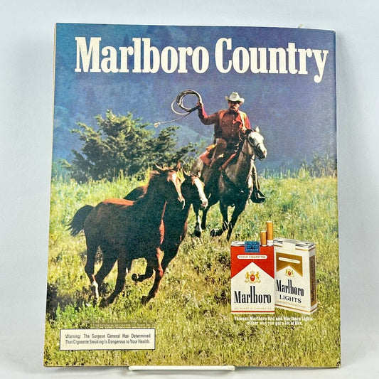 A vintage Marlboro Country cigarette advertisement featuring a cowboy riding a horse chasing other horses. 