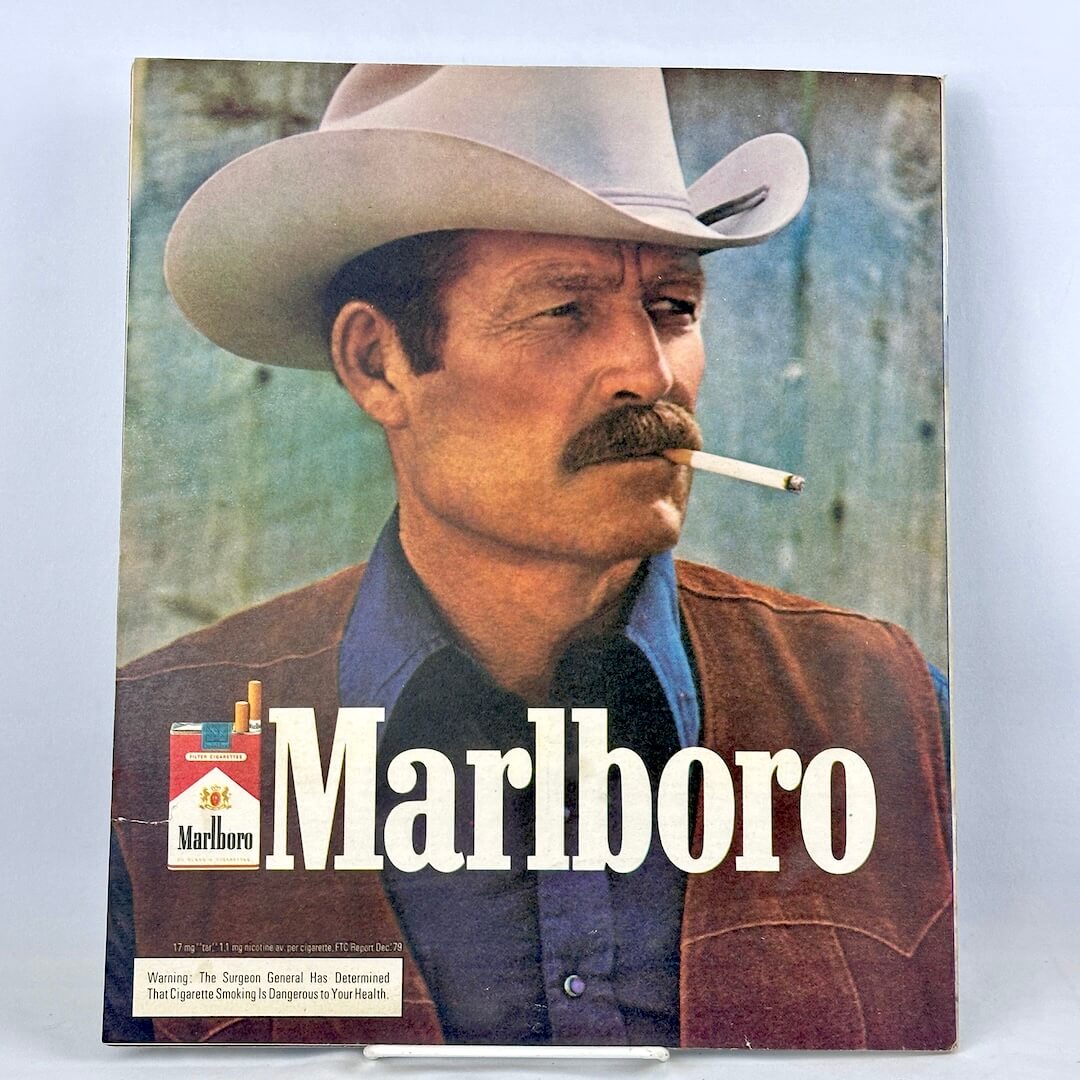 Vintage Marlboro cigarette ad featuring a cowboy in a white hat and brown vest smoking a cigarette.