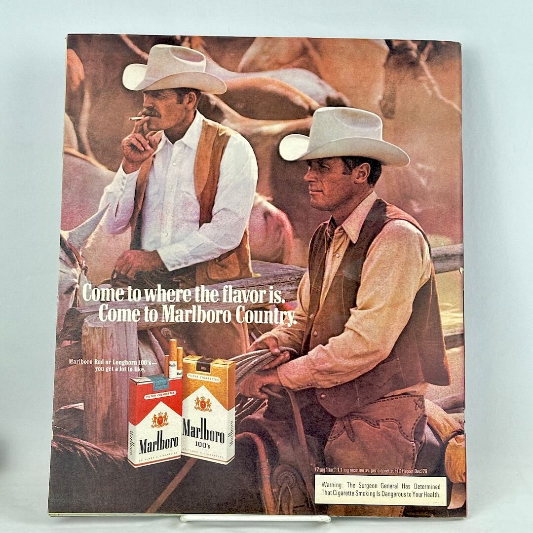 A vintage Marlboro Country magazine ad featuring two cowboys in a dusty western setting, with two Marlboro packs.