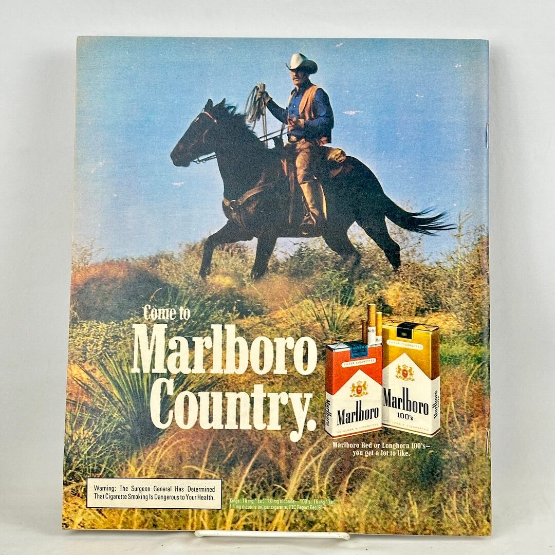 Back cover of magazine with full page Marlboro ad featuring mounted cowboy riding through field. 