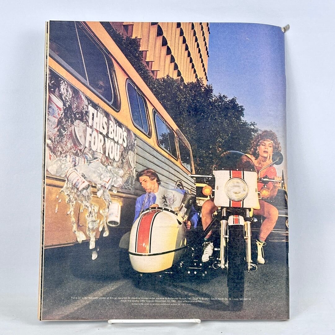 Back cover of magazine featuring an ad with woman riding motorcycle with man in sidecar riding alongside a bus.