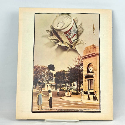 Back cover with full page Budweiser ad with photo of a town square with a beer can appearing to bust out of the page. 