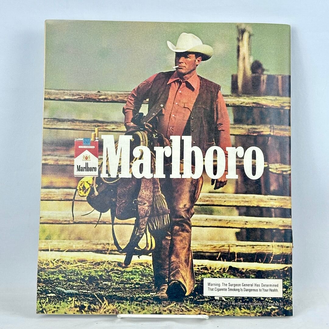 Back cover of magazine featuring full size Marlboro ad with photo of cowboy smoking carrying a saddle. 