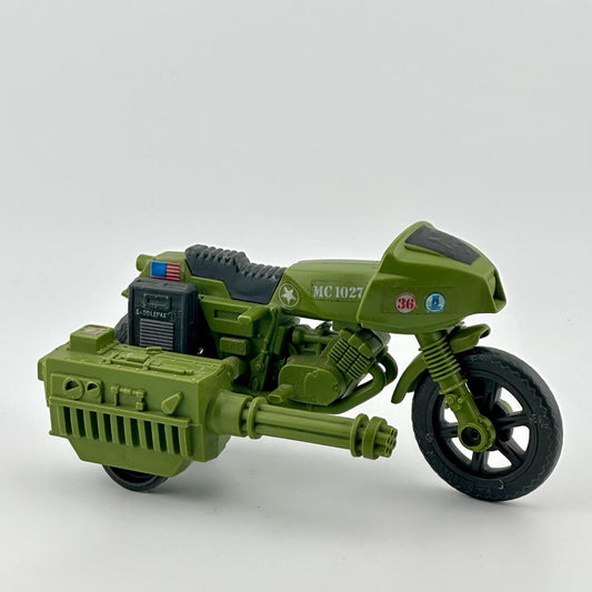 Army green motorcycle with grey carry cases on either side & grey seat, big gun, & G.I. Joe & American flag sticker decals. 