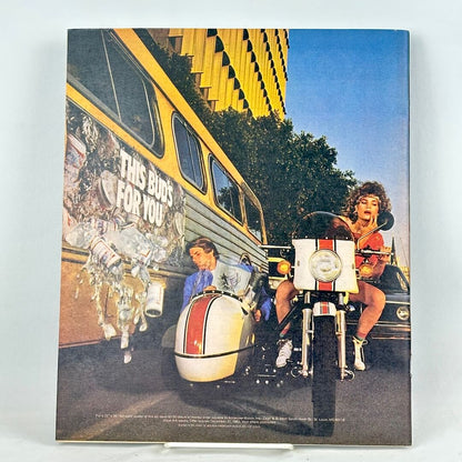 Back cover of magazine showing an ad with woman riding a white motorcycle with a sidecar next to a yellow bus.