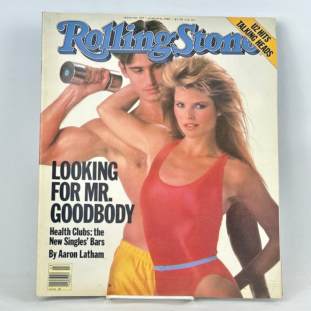 A vintage Rolling Stone magazine cover featuring a shirtless man lifting a barbell behind a woman in a red swimsuit