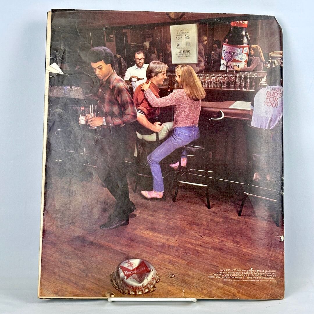 Back cover of magazine with full page ad for Budweiser featuring an image of people interacting at a bar. 