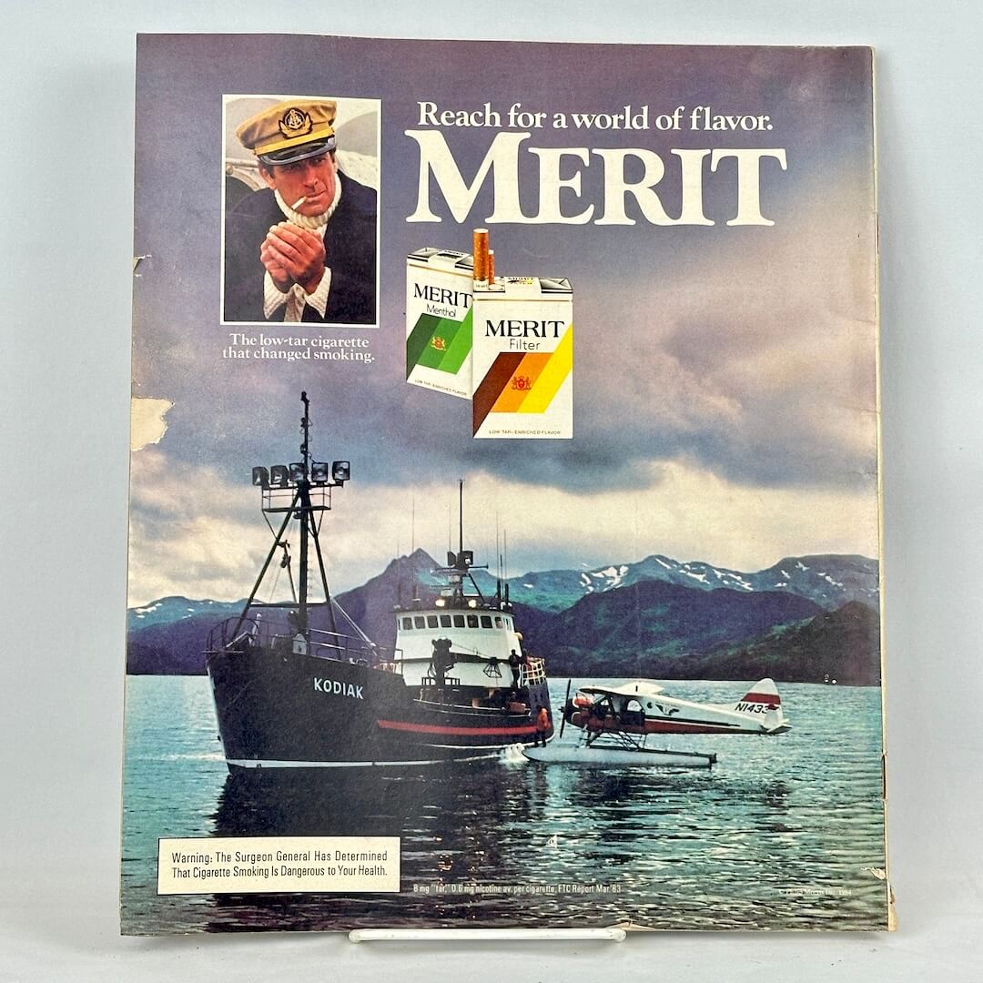 Back cover of magazine with full page ad for Merit cigarettes featuring image of boat and plan on mountain lake. 