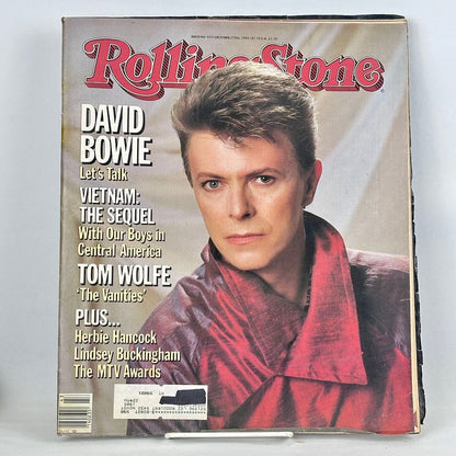 Vintage issue of Rolling Stone magazine with portrait of David Bowie wearing red on beige background. 