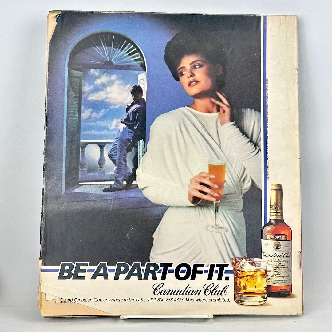 Back cover of magazine with full page ad for Canadian Club whiskey with woman holding a glass with man in background. 
