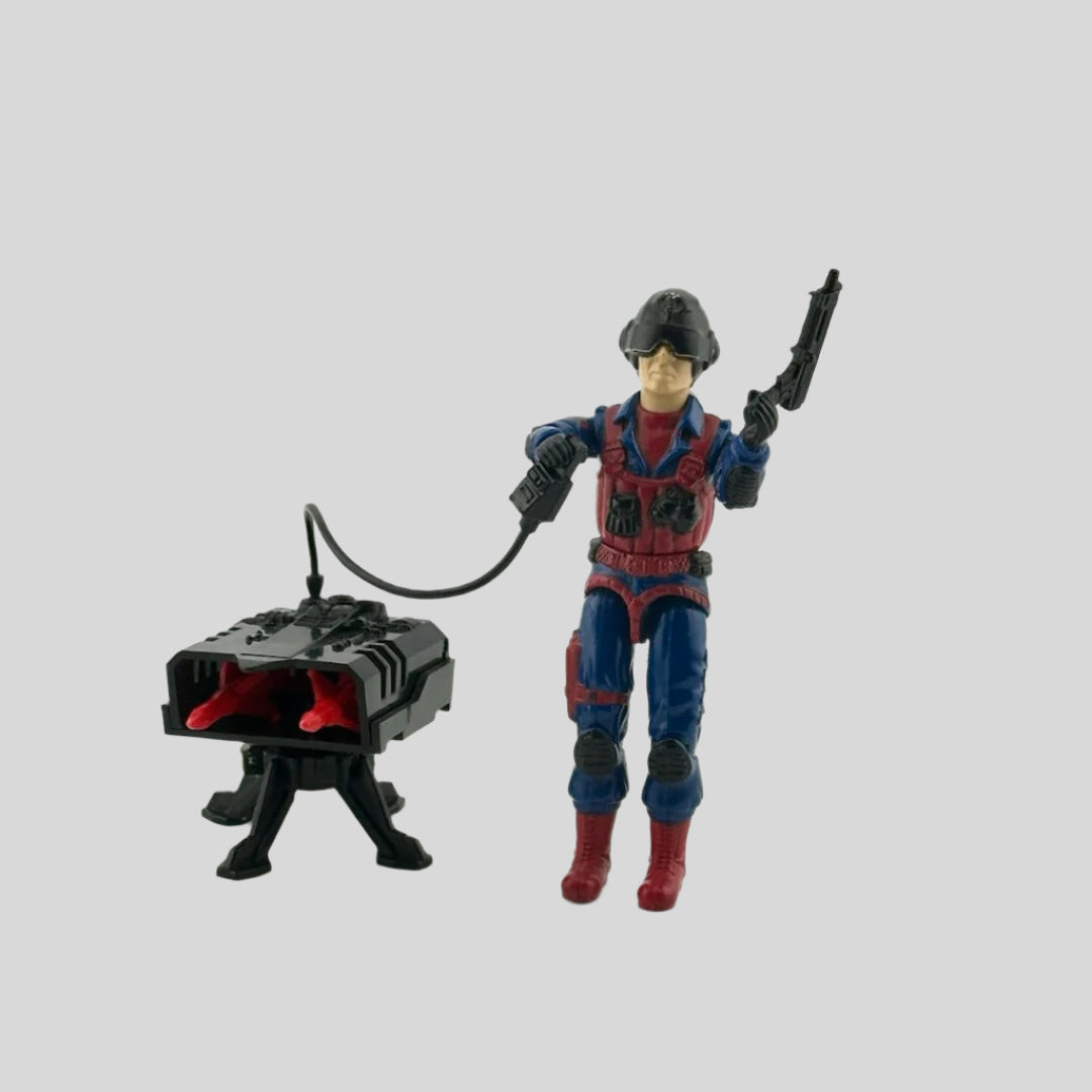 White male action figure in blue suit with red details, wearing black helmet, holding gun & trigger to missile box accessory.