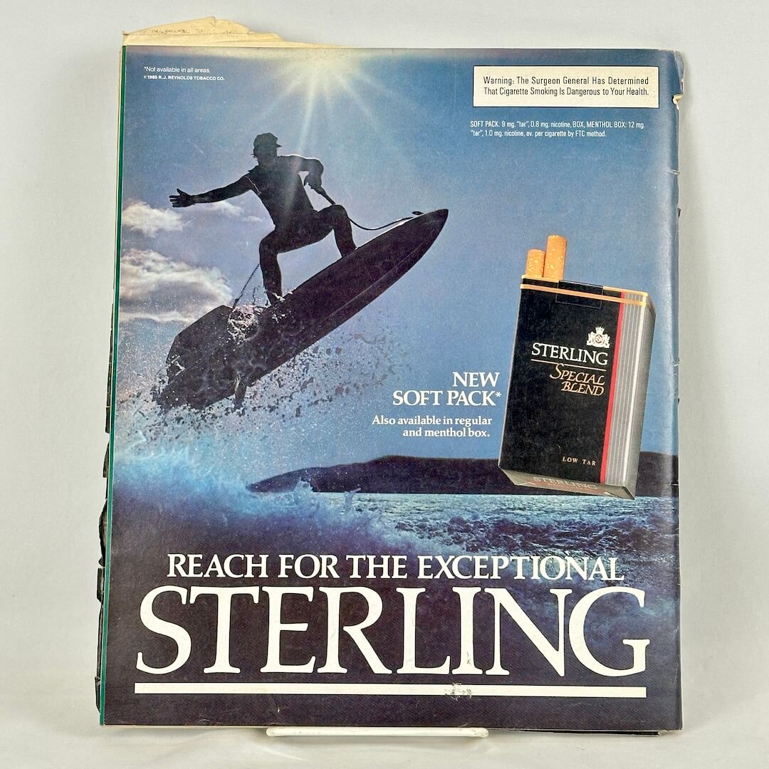 Back cover of magazine with full page ad for Sterling cigarettes featuring image of surfing guy and pack of smokes. 