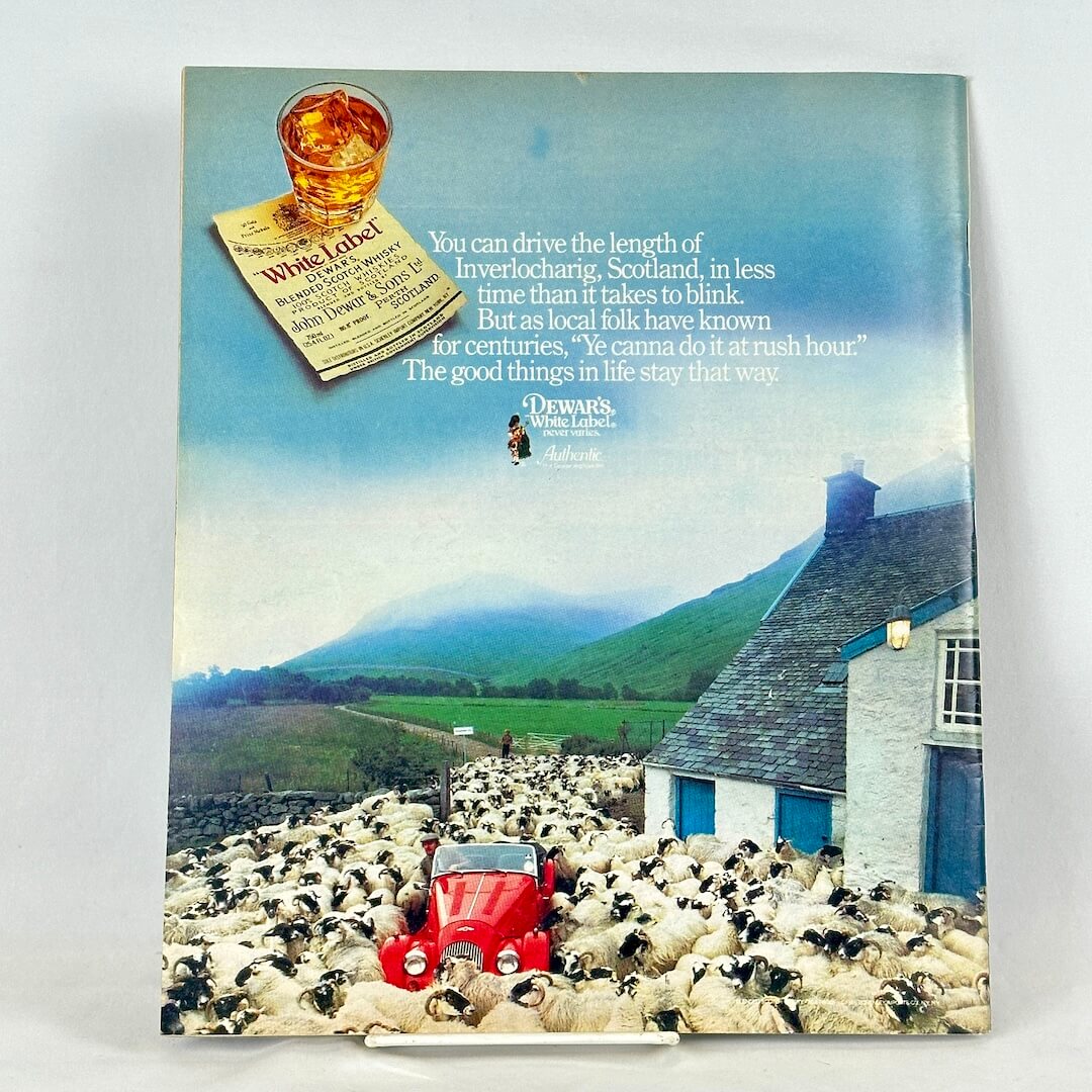 Back cover of magazine with full page ad for Dewar's White Label with image of red car among herd of sheep.