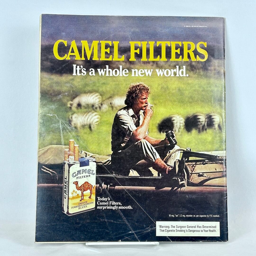 Back cover of magazine with full page ad for Camel cigarettes featuring image of man sitting in car smoking among zebras.