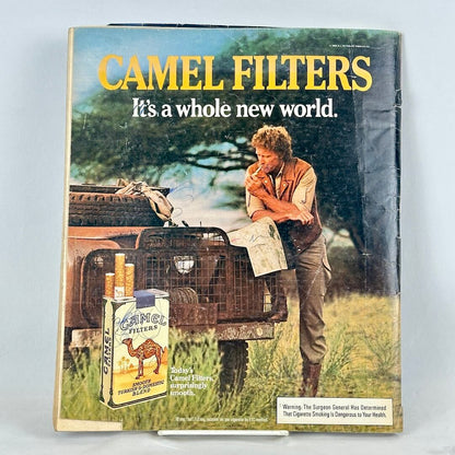 Back cover of magazine with full page ad for Camel cigarettes featuring man smoking and leaning on car by tree. 
