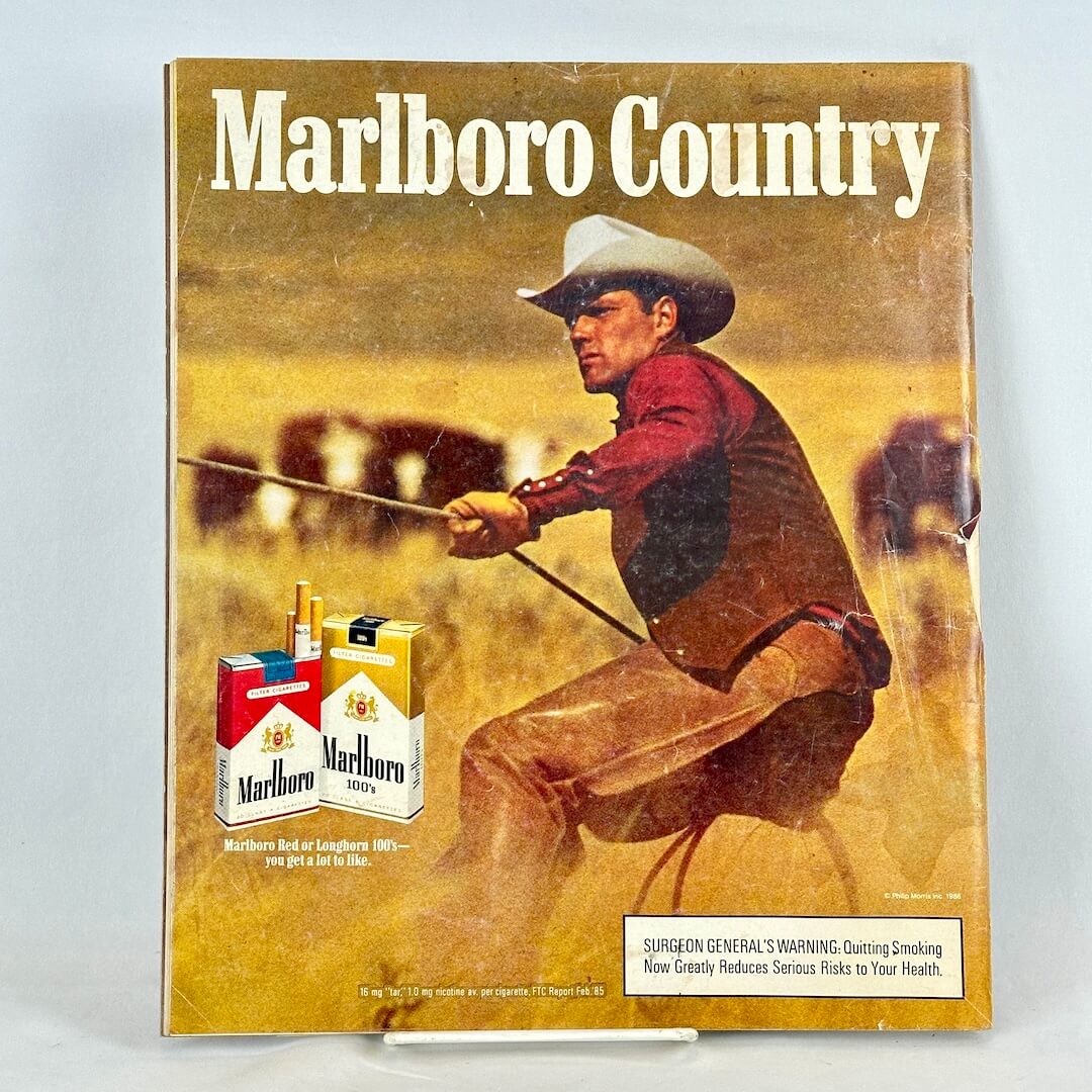 Back cover of magazine with full page ad for Marlboro cigarettes featuring a cowboy with a rope in a wheat field. 