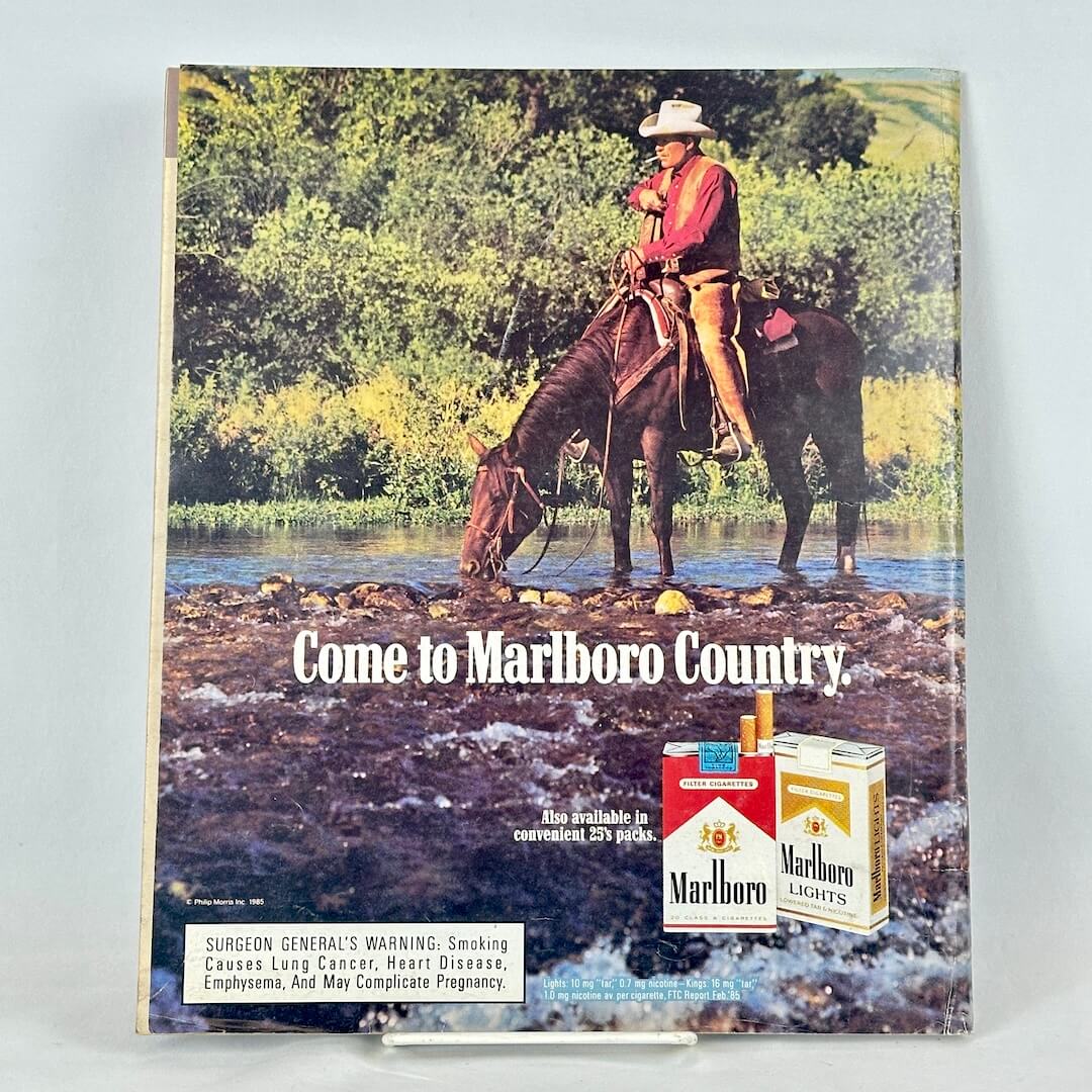 Back cover of magazine with full page ad for Marlboro cigarettes featuring a mounted cowboy, smoking in a stream.