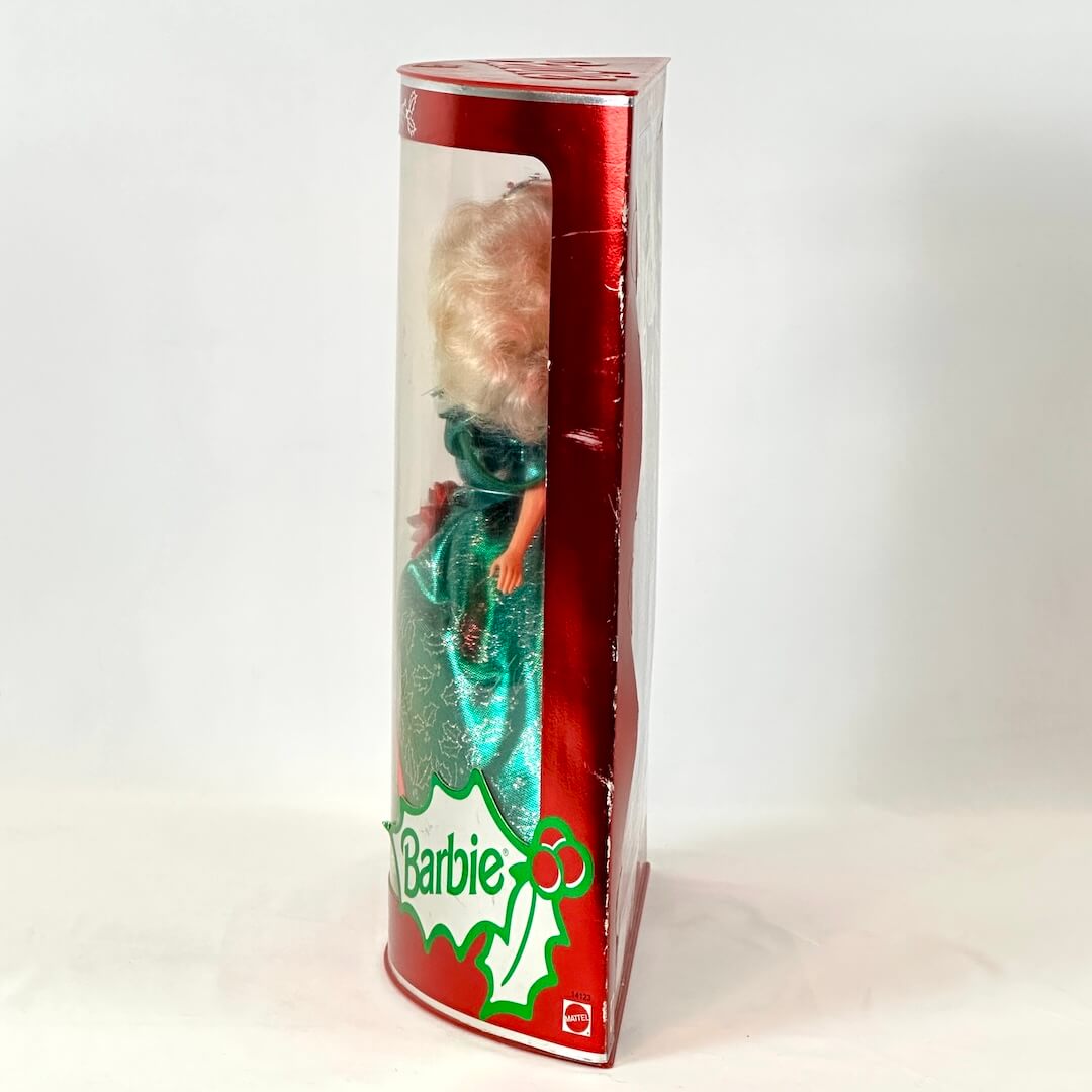 Barbie doll in a green dress inside a red and white box with 'Barbie' branding.