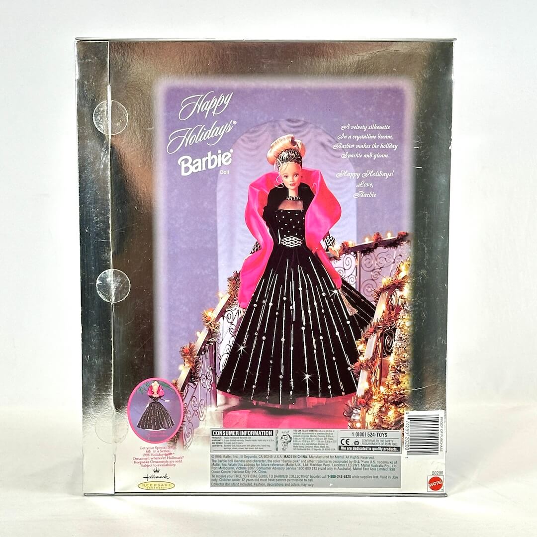 Barbie doll in a festive outfit with pink cape and black dress, surrounded by Christmas decorations on packaging.