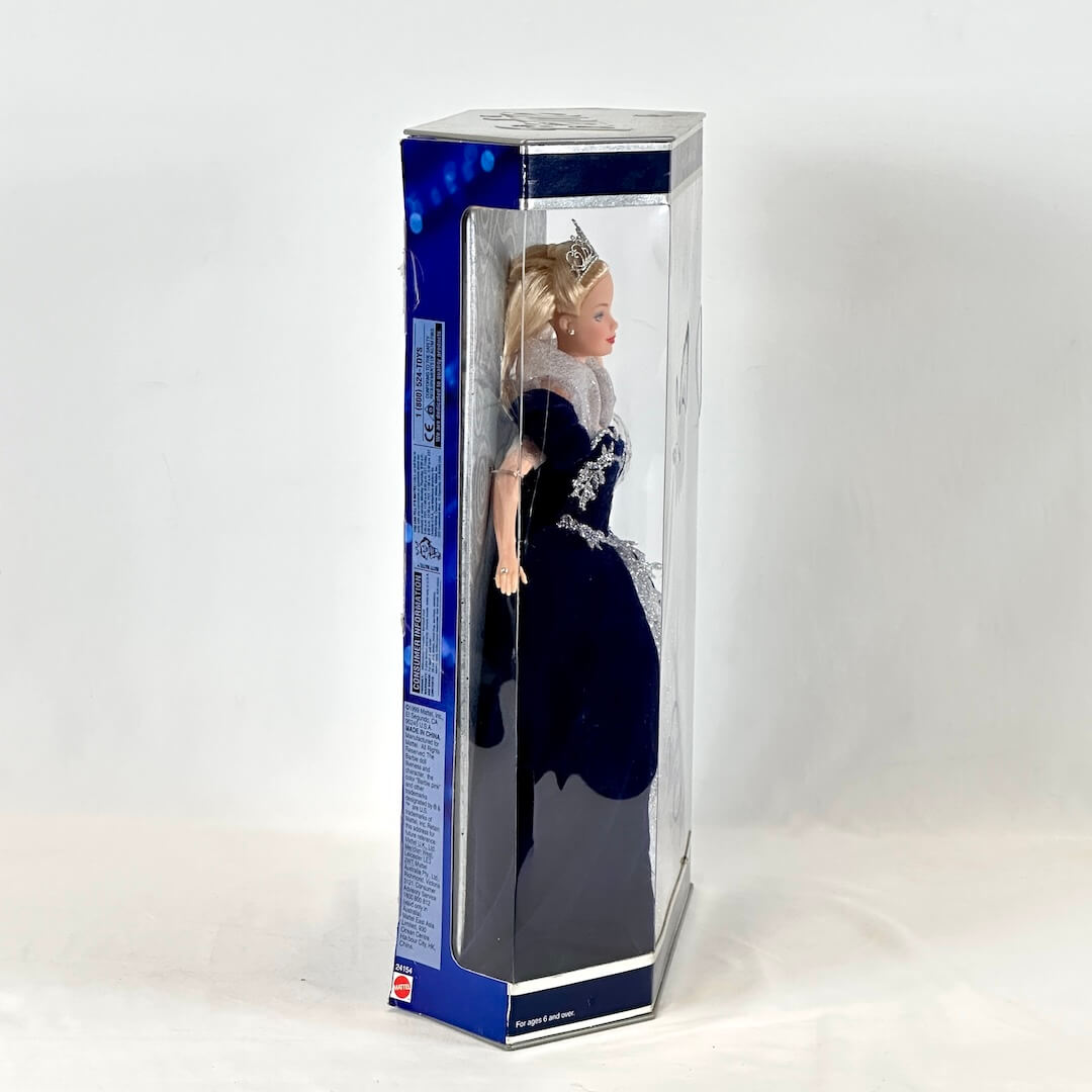 Doll in a blue dress with a tiara inside a clear box on a white background