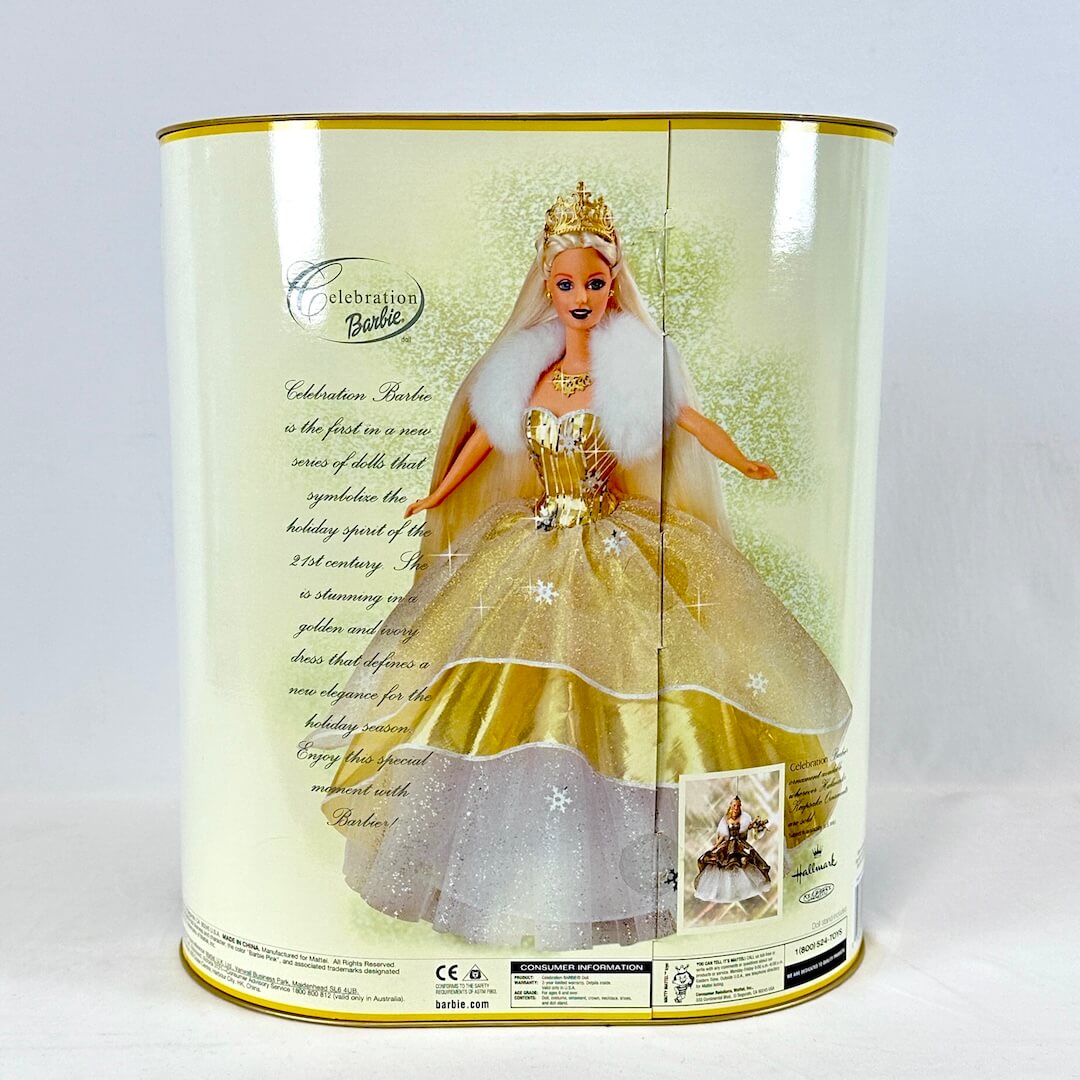 Barbie doll in a gold dress with a white cape inside a cylindrical packaging box.