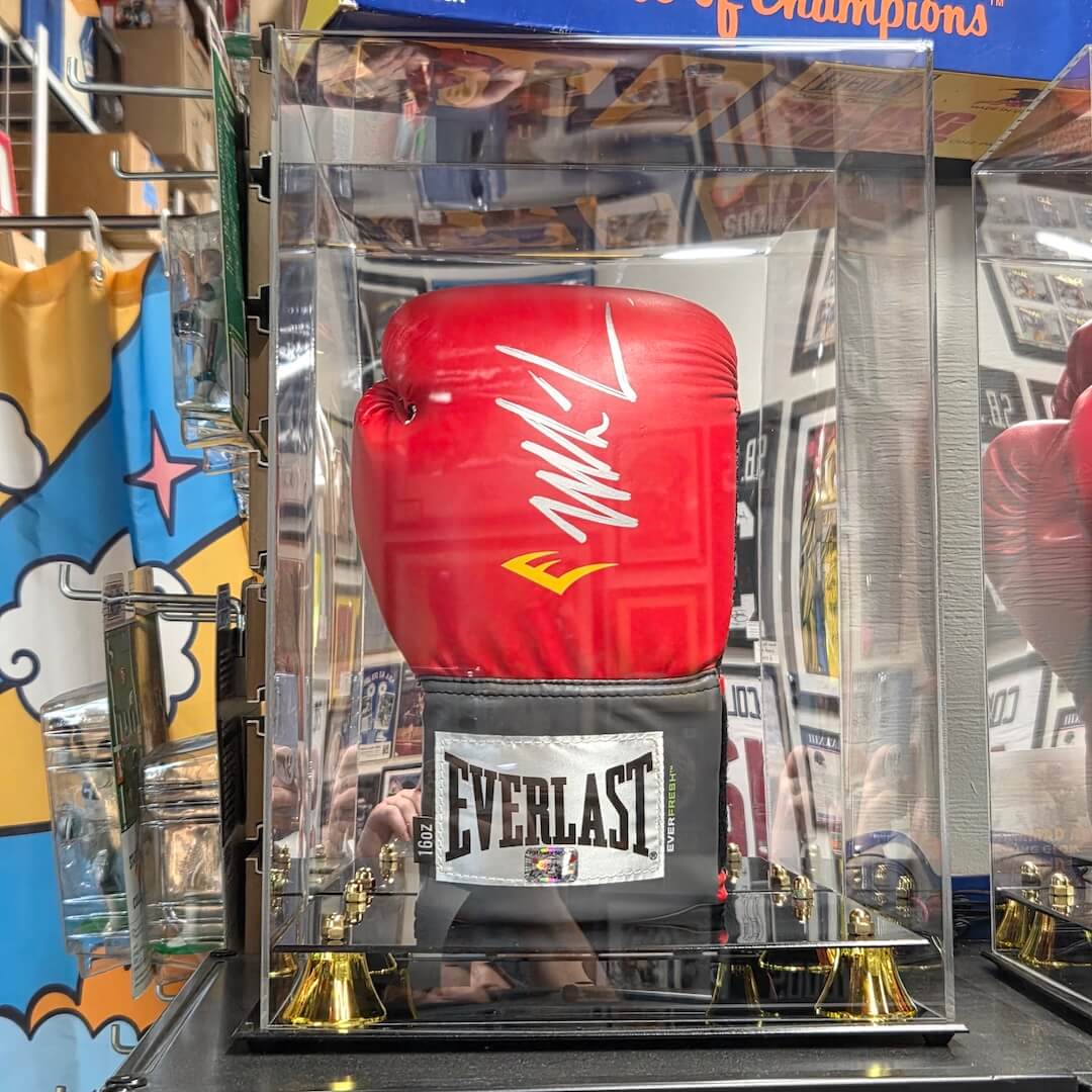 A red Everlast boxing glove with a white signature on the wrist strap, displayed inside a clear acrylic case on a mirrored base with gold bells.