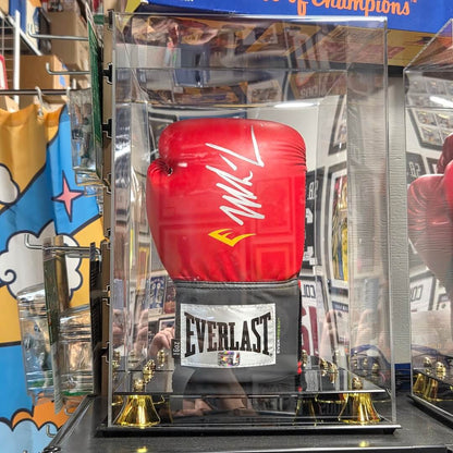 A red Everlast boxing glove with a white signature on the wrist strap, displayed inside a clear acrylic case on a mirrored base with gold bells.