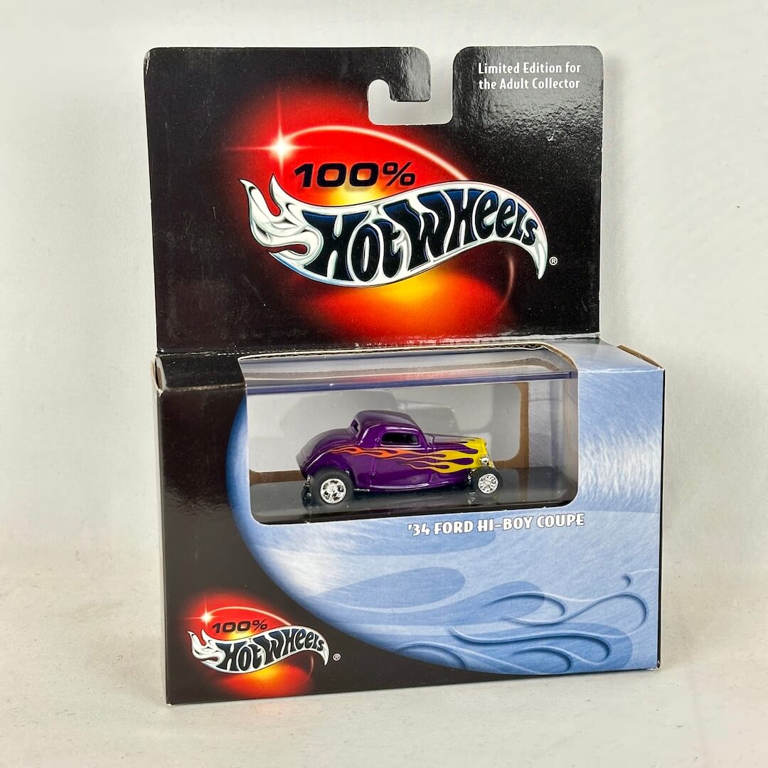 A Hot Wheels 1964 Ford Hi-Roar Coupe diecast toy car in its original packaging, featuring a purple body with flame decals.