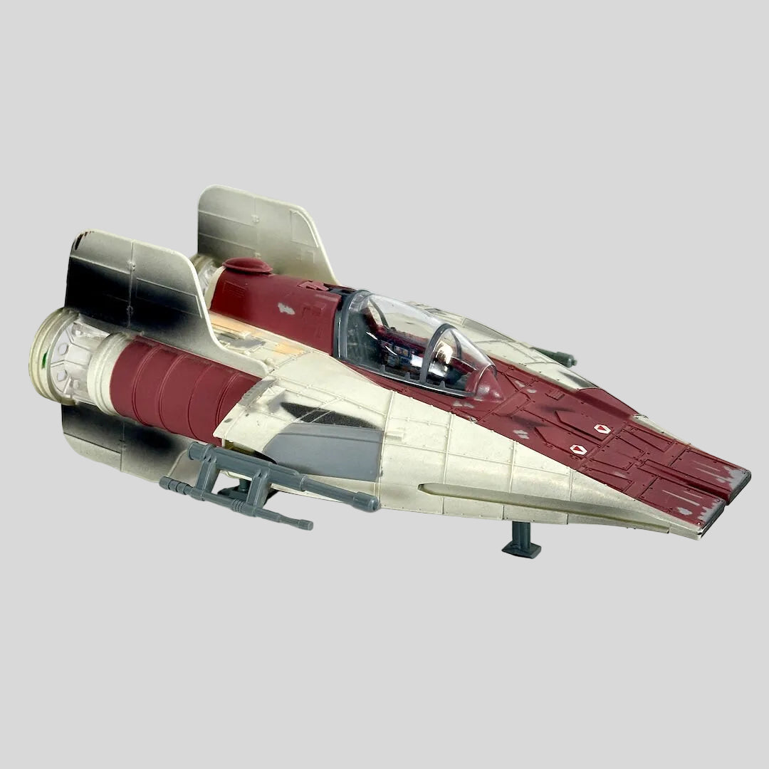 A toy futuristic starfighter spacecraft, featuring a cream and dark red color scheme with gray engine components.