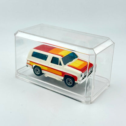 Model of a vintage Blazer with a colorful design inside a clear display case on a light gray background