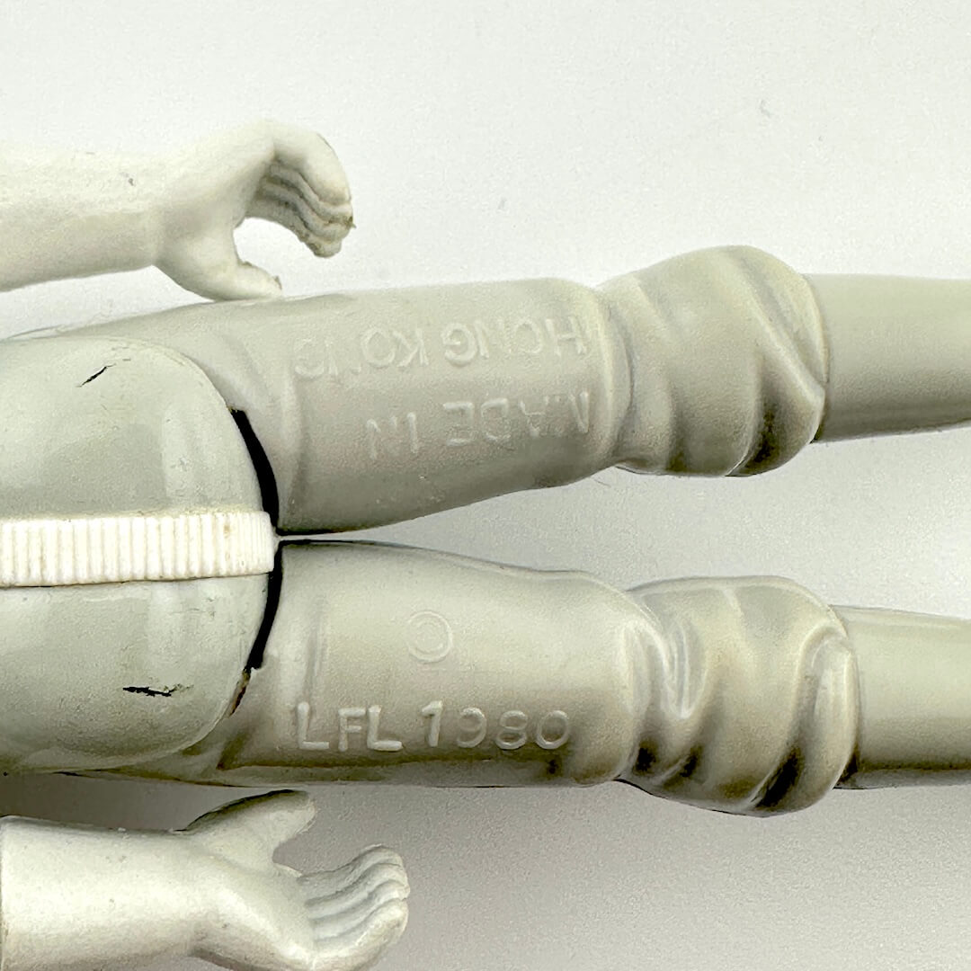 Close-up of a white plastic figure with visible branding on a light gray background