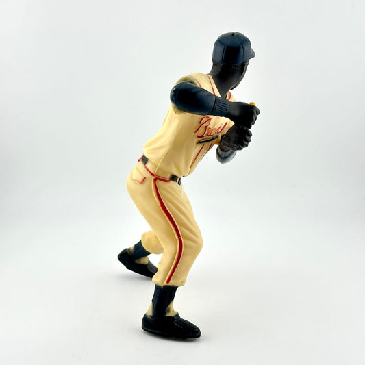 Baseball player in cream uniform with red writing in mid-batting pose with missing bat. 