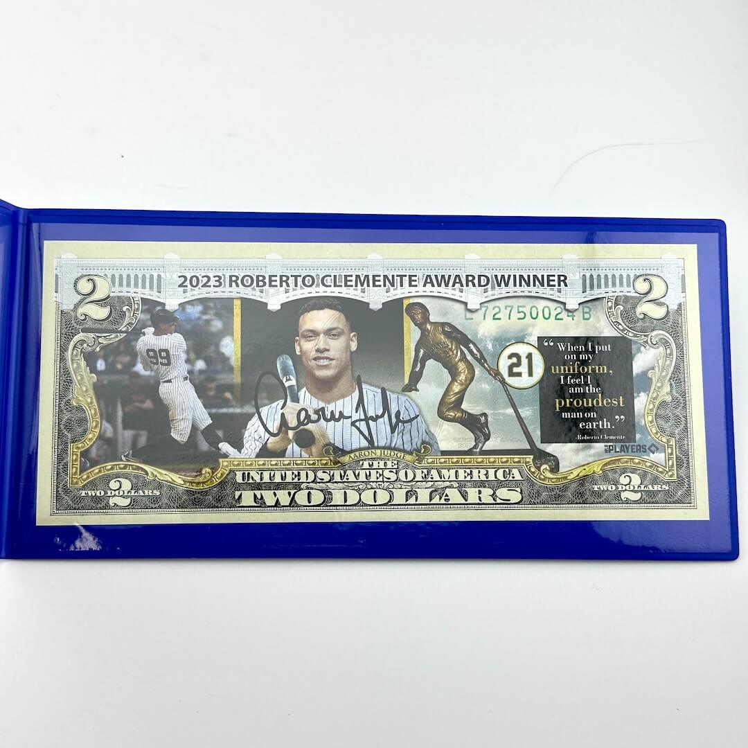 Two-dollar bill with a blue border featuring a sports-themed design and text.