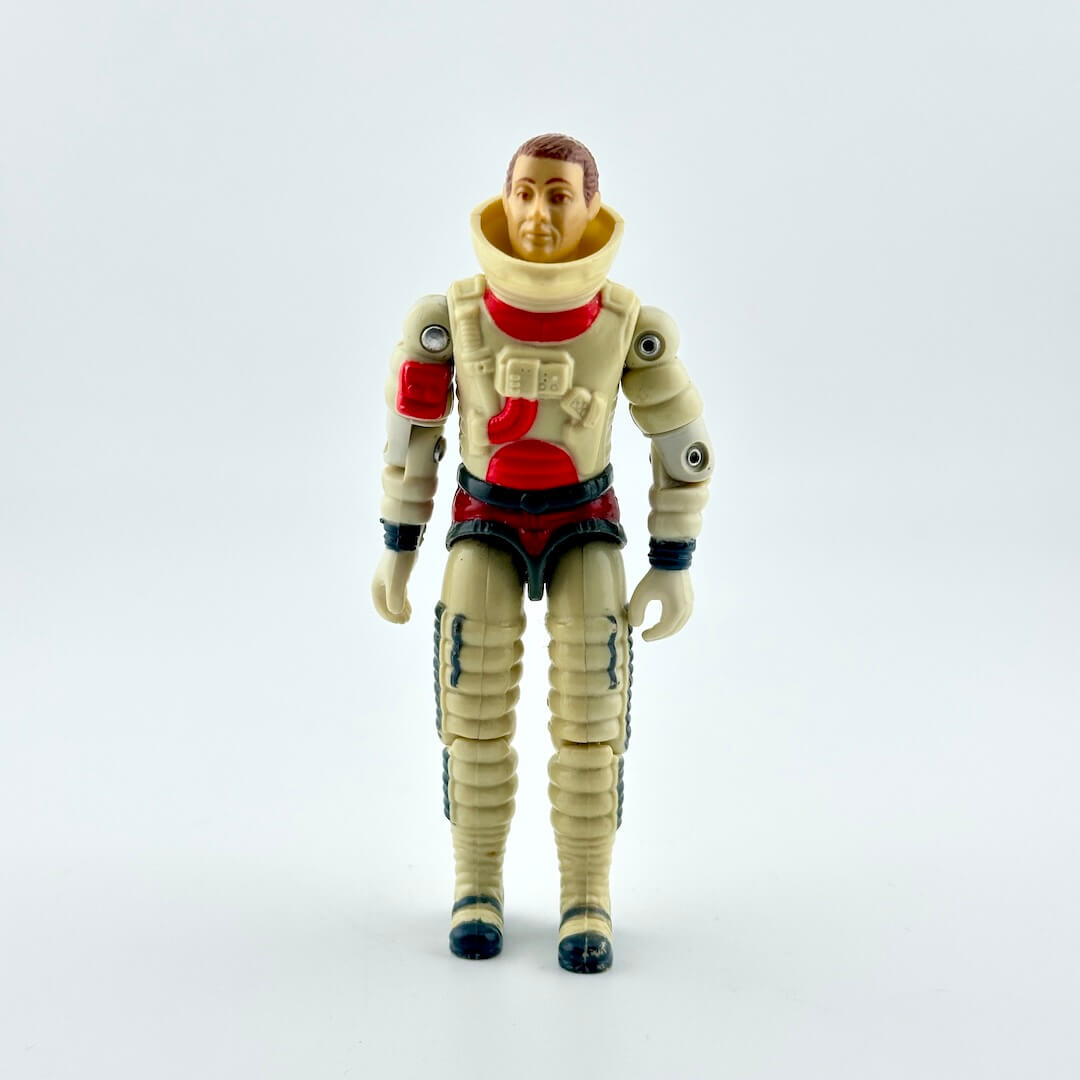 A vintage plastic astronaut action figure standing against a seamless light gray background. 